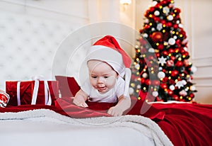 Newborn baby creeps on bed, wearing Santa hat. Baby in a Christmas Santa cap