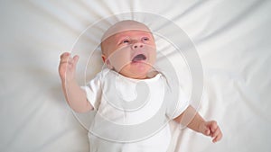a newborn baby cries on a white sheet. childish tantrums. top view.