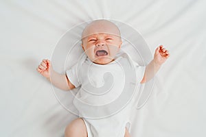 a newborn baby cries on a white sheet. childish tantrums. top view.