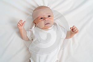 a newborn baby cries on a white sheet. childish tantrums. top view.