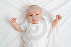 a newborn baby cries on a white sheet. childish tantrums. top view.