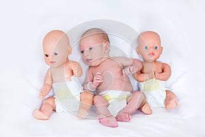 Newborn baby in diaper between two plastic dolls