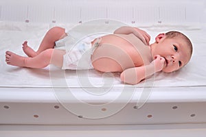 A newborn baby in diapers on a white changing table with a ruler for measuring full height