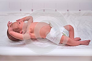 A newborn baby in diapers on a white changing table with a ruler for measuring full-length photo