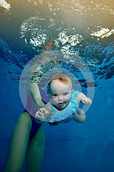 A newborn baby dives under the water in a children`s pool on a blue background. Mother teaches the baby to swim. Fashion