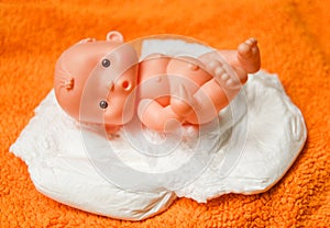 Newborn baby doll with Diapers - baby toy wear white diaper and playing on a orange knitted blanket in the nursery concept