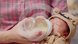 Newborn baby drinking milk from bottle on mom arms.Beautiful Asian mother holding infant baby feeding milk with love at home.