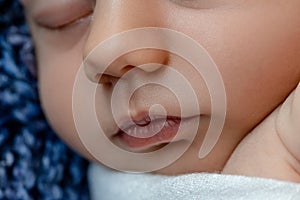 Newborn - baby, face close-up. The sleeping Newborn boy under a white knitted blanket lies on the blue fur.