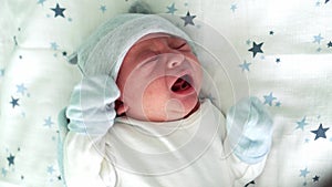 Newborn Baby Face Portrait Early Days On Back Crying At White Blue Star Background. Child At Start Minutes Of Life on