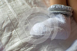 Newborn baby feet close up. Baby feet in white terry socks, baby lying on bed, baby`s legs, Newborn