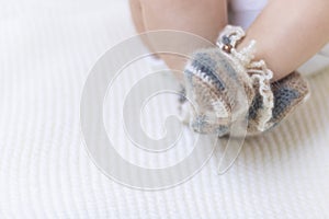 Newborn baby feet close up in wool brown knitted socks booties on a white blanket. The baby is in the crib