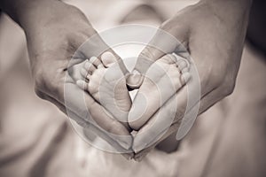 Newborn baby feet in its mother`s hands shaped like a heart. Mother showing her love and affection. Monochrome