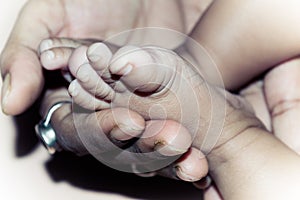 Newborn Baby Feet in Mother Hands. Beautiful infant little baby fingers and foot in mother`s palm. Close-up. Child health care an