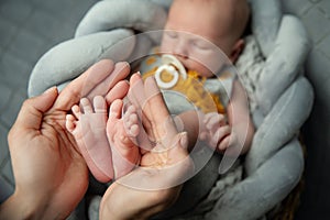 Newborn Baby Feet in Mother Hands. Mom holding sleeping Baby Legs in Arms. New Born Child Foot close up. Parent Love and Health
