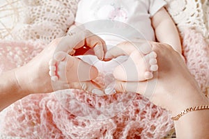 Newborn baby feet in mother hands, shape like a lovely heart. Mother holding legs of the kid in hands. Close up image. Happy