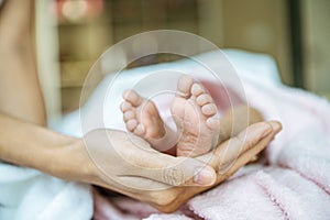 Newborn baby feet on the mother`s hand on a white blanket