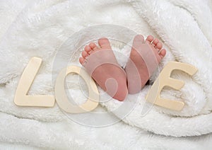 Newborn baby feet under white a blanket with love text.