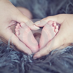Newborn baby foot in mother hand detail. Baby care. Parents holding baby feet in hand like heart-shaped.