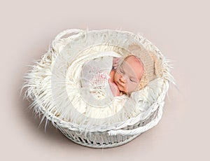 Newborn baby in funny bonnet napping in basket