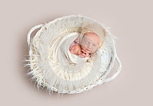 Newborn baby in funny bonnet napping in basket