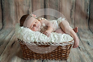 Newborn baby girl in bandage bow sleeping in wicker basket on plaid shawl on beige wooden floor