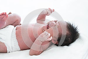 Newborn baby girl crying and screaming, lying on bed at home. Asian Australian infant 19 days old wear diaper, showing unhappy