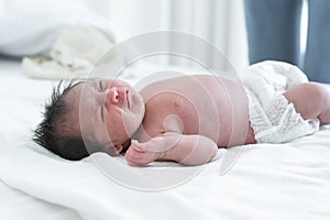 Newborn baby girl crying and screaming, lying on bed at home. Asian Australian infant 19 days old wear diaper, showing unhappy