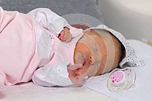 Newborn baby girl dressed in a pink sleep suit. The baby girl is 15 days old