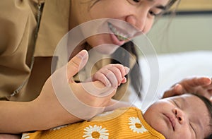 Newborn baby girl holding mother hand. Smiling mom and child on white bed