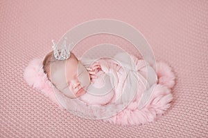 Newborn baby girl in a pink cocoon on a pink background, sleeping princess with a crown