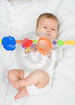 Newborn baby girl playing with toy rattle lying on back