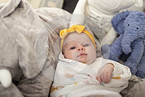 Newborn baby girl posing with a twinkle in her eyes and wearing a yellow bandanna with yellow bow..