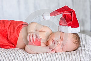 Newborn baby girl in red santa hat sleeping with a gift in hands