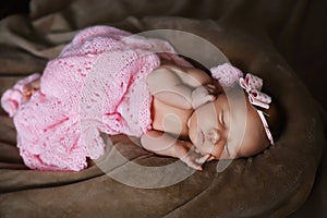 Newborn baby girl sleeping cute, covered with soft pink scarf, neatly folded under a pen with a small head with a pink bow, set
