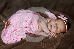 Newborn baby girl sleeping cute, covered with soft pink scarf, neatly folded under a pen with a small head with a pink bow, set