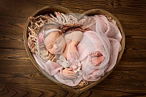 Newborn baby girl sleeping in a pink wrap with a pink flower on her head.