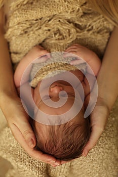 Newborn baby girl sleeping under cozy blanket in mom's hands