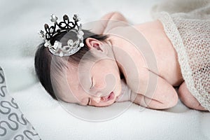 Newborn baby girl sleeping and wearing a silver crown.