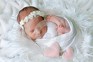 Newborn baby girl sleeping on white fur background in cocoon with toy heart, place for text, healthy baby sleep