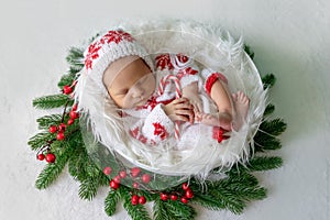 Newborn baby girl sleeping on white fur background under Christmas tree with candy in hand, place for text, healthy baby sleep,