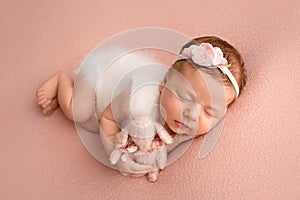 Newborn baby girl sleeping in a white jumpsuit with pink rabbit a white bandage