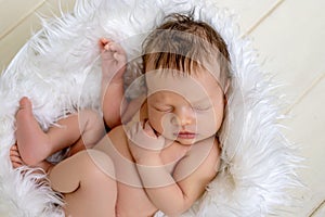 Newborn baby girl two weeks sweetly sleeping in a basket with white fur on the background of a wooden floor