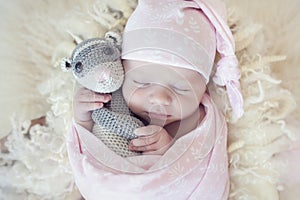 Newborn baby girl wrapped in pink wrap with flower pattern on wool fluffy blanket. Sweet infant sleeping in props for