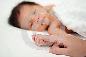Newborn baby hand holding index finger of mother on bed