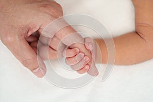 Newborn baby hand holding index finger of mother on bed