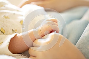 Newborn baby hand in mother`s hands with soft light blue blanket