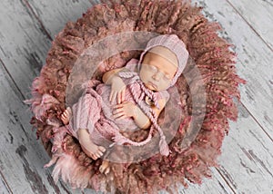 Newborn baby in hat and jumpsuit sleeping in round bed