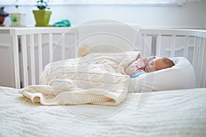 Newborn baby having a nap in co-sleeper crib attached to parents` bed