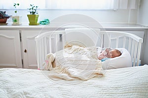 Newborn baby having a nap in co-sleeper crib attached to parents` bed