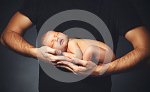 Newborn baby in his father`s hands in dark